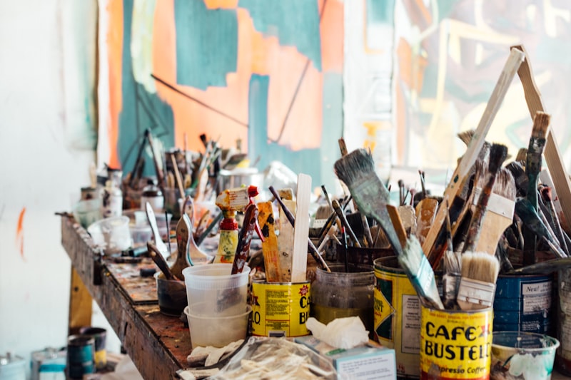 Brushes and jars of medium crowded on a paint spattered bench.