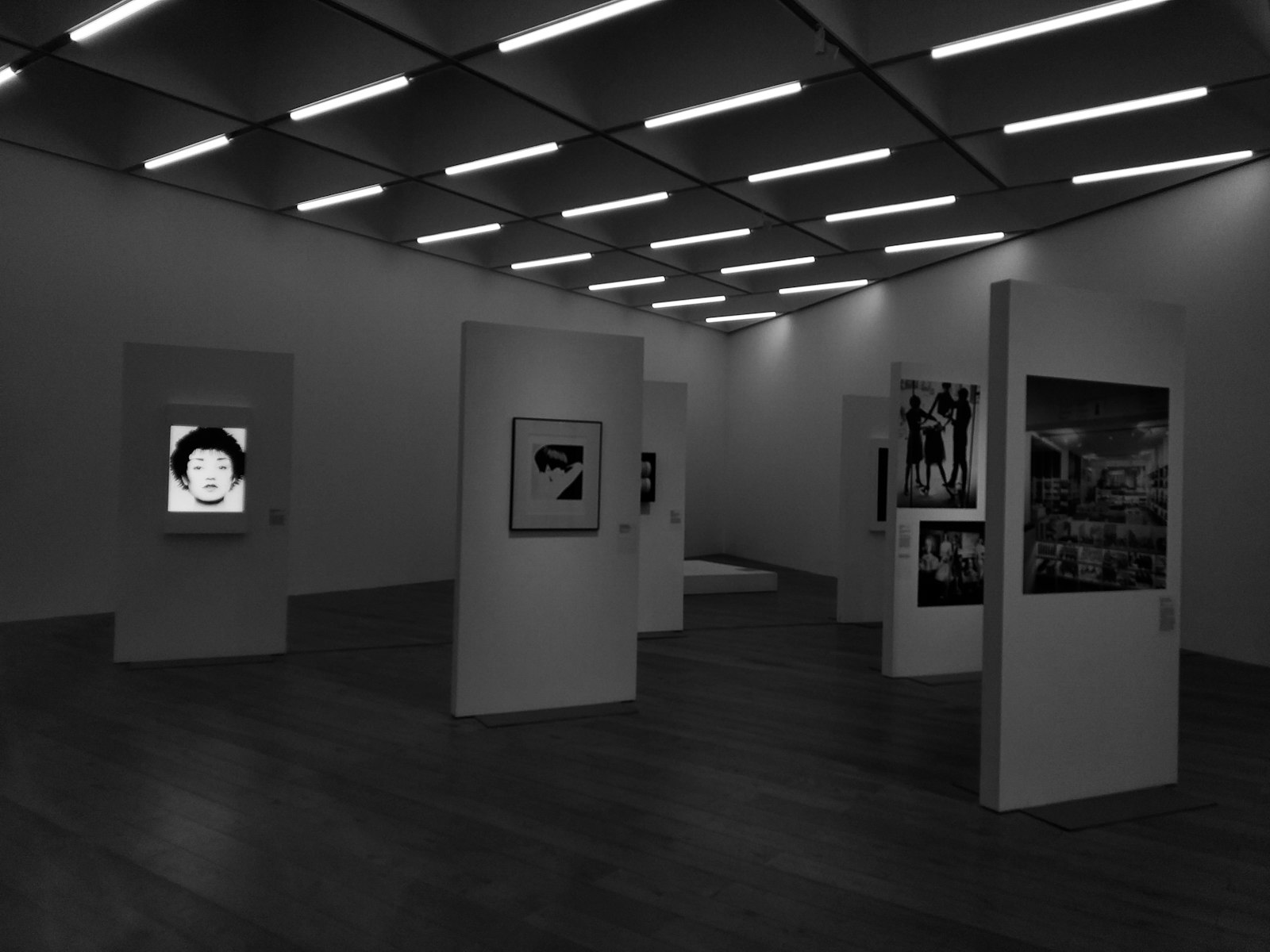 A grey walled gallery with framed works spaced along freestanding partitions.