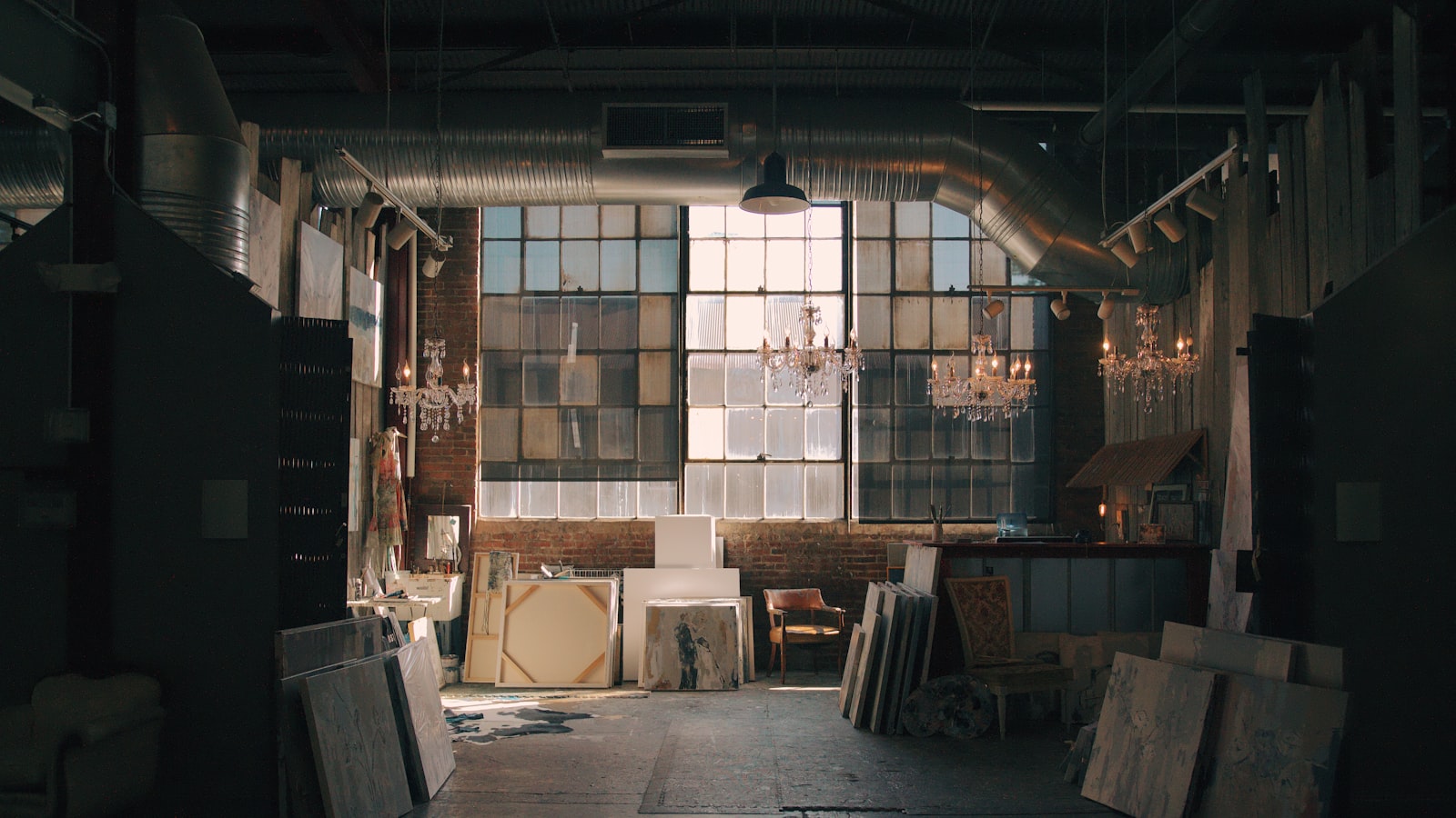 A large industrial studio hall with tall windows and stacked panels leaning against the wall.