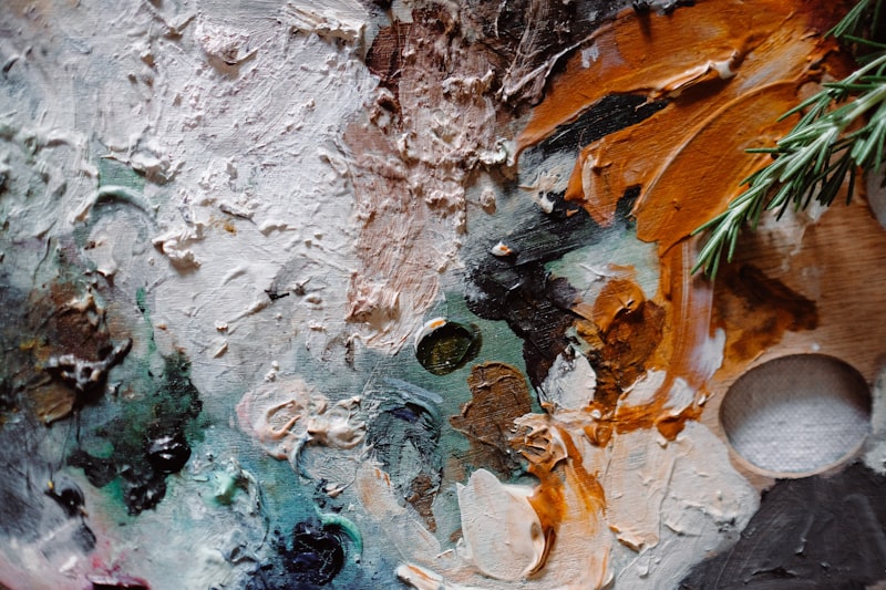 A close view of thick impasto paint in teal, rust and white on a canvas surface.