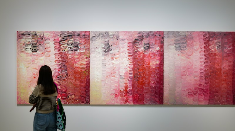 A visitor standing in front of a wide multi panel painting in a gallery.